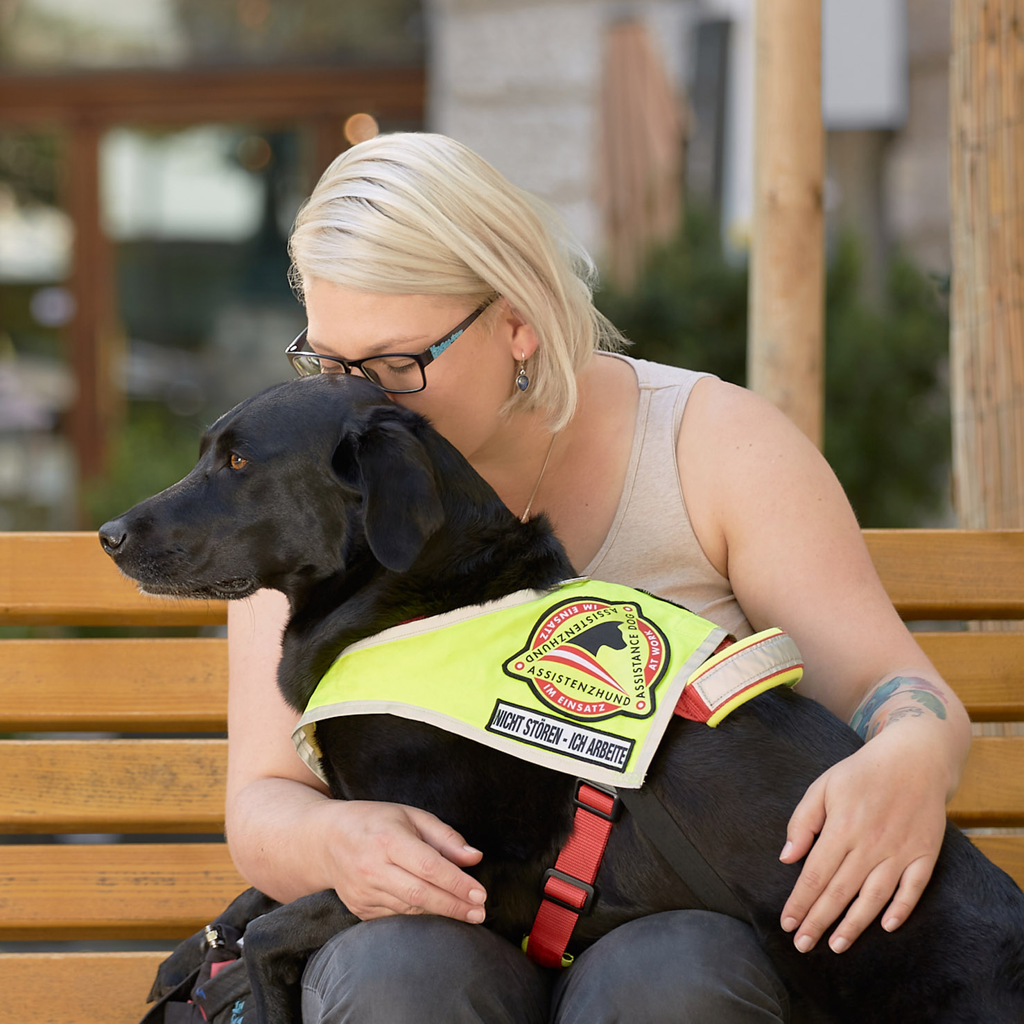 Ein Signalhund (schwarzerLabrador) liegt auf dem Schoß seines Menschen für eine Deep Pressure Therapy.