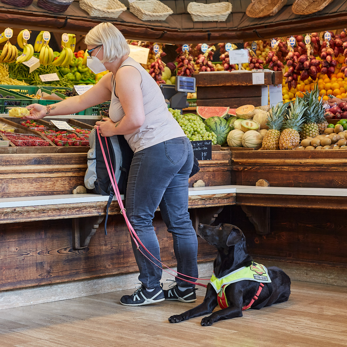 Ein Signalhund (schwarzer Labrador) liegt im Supermarkt bei seinem Menschen, um Abstand zu schaffen.